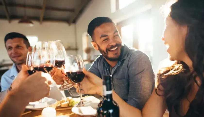 Des amis trinquent avec des verres de vin rouge lors d'une soirée dégustation vin conviviale, riant sous le soleil.