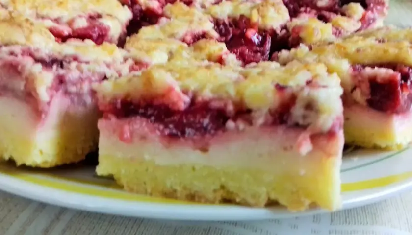 Pyszne ciasto z truskawkami i budyniem, z kruszonką na wierzchu, pokrojone na kwadraty, leży na talerzu.
