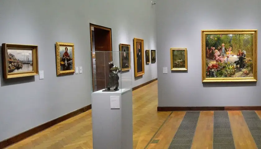 Obraz przedstawia galerię sztuki. Na ścianie wisi obraz z żydówką z pomarańczami.