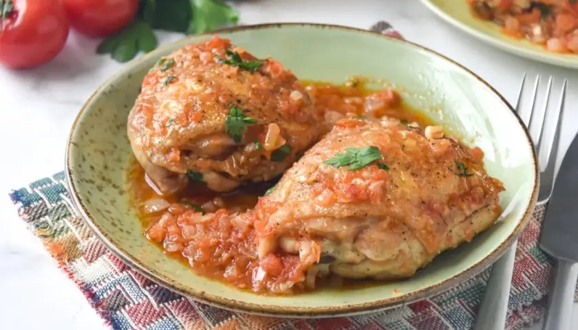 Dos jugosos contramuslos de pollo en salsa de tomate y cebolla, adornados con perejil fresco. Un plato casero y reconfortante.