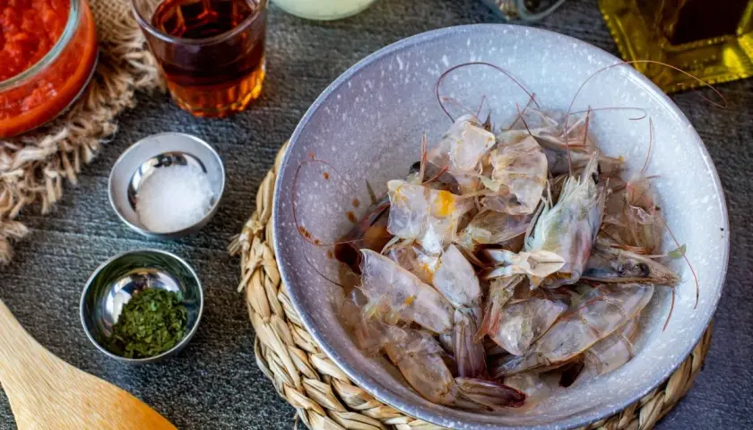 Cáscaras de camarón en un tazón, listas para hacer una sabrosa salsa americana. Ingredientes como tomate triturado, sal y hierbas acompañan.
