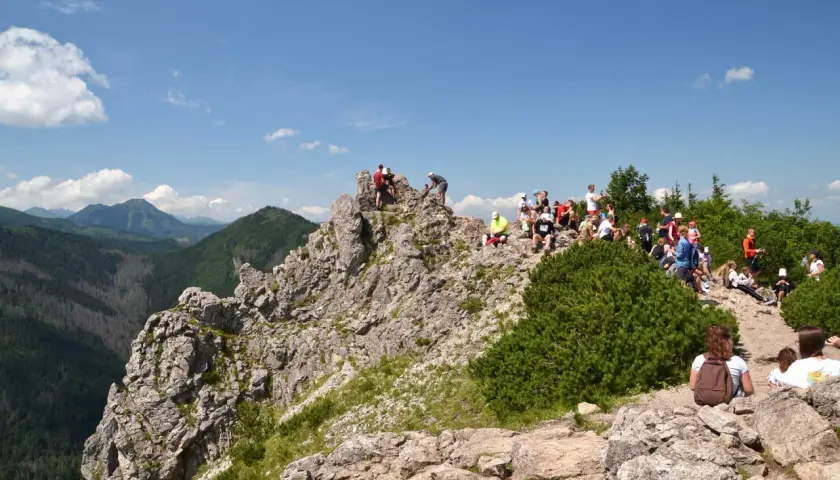 Grupa turystów odpoczywa na skalistym szczycie, podziwiając widok na dolinę Białego Potoku.
