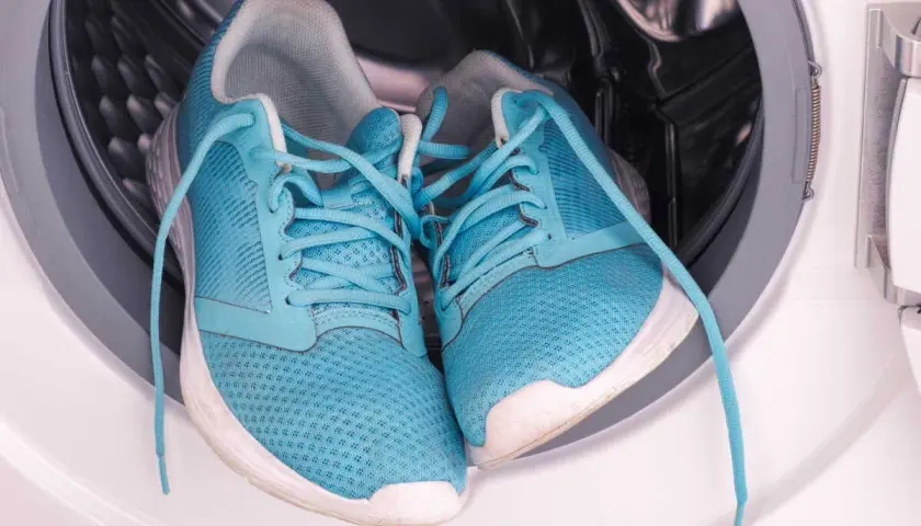 Paire de baskets bleues dans le tambour d'une machine à laver. Prêtes pour un cycle de nettoyage.