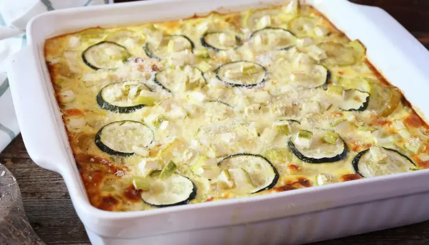 Pyszna zapiekanka z cukinii i mięsa mielonego, posypana parmezanem, w białym naczyniu żaroodpornym.