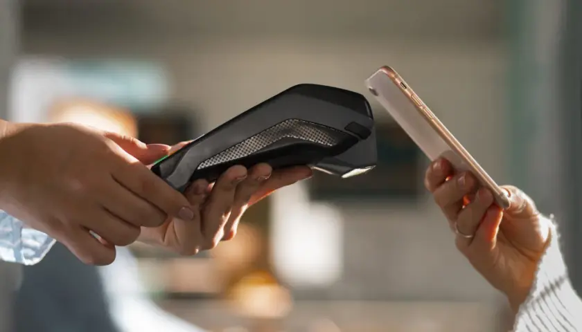 Dwie dłonie zbliżają do siebie telefon i terminal płatniczy. Pokazuje to, jak placic telefonem w prosty i szybki sposób.