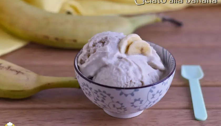 Una ciotola di cremoso gelato alla banana, guarnito con fettine di banana, accanto a banane fresche e un cucchiaino.