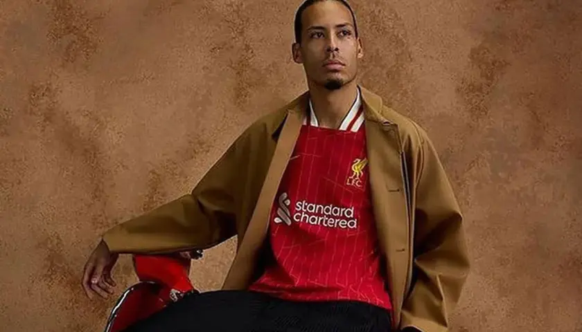 Mężczyzna w brązowej marynarce i czerwonej koszulce Liverpool z logo Standard Chartered.