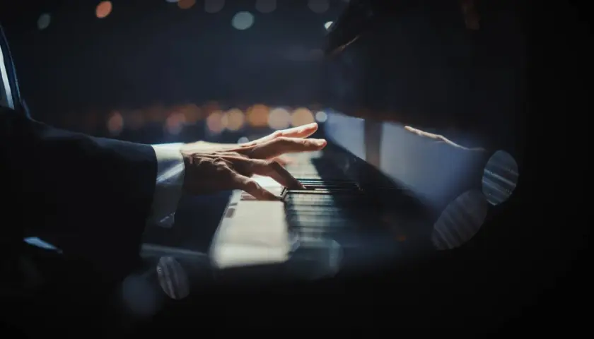 Dłoń pianisty grająca nokturn na fortepianie, w tle rozmyte światła.