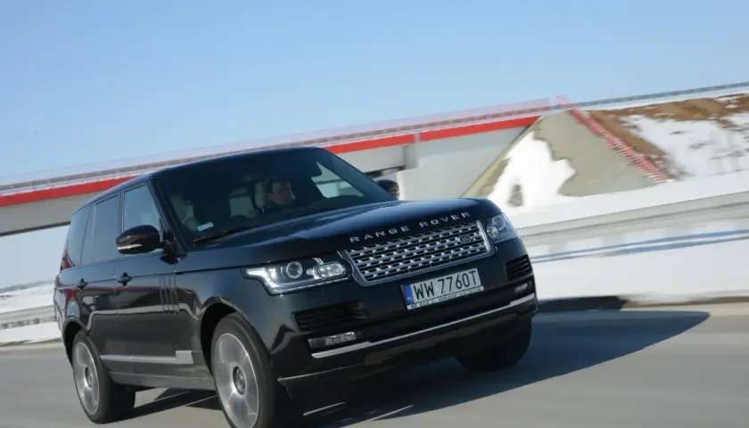 Czarny Range Rover Vogue pędzi po drodze, za nim śnieżne krajobrazy i błękitne niebo.