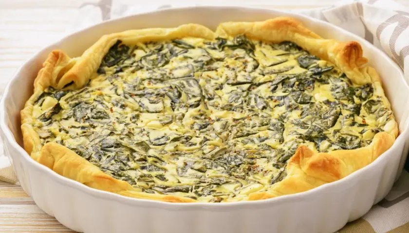 Pyszny quiche ze szpinakiem w białej formie, idealny pomysł na to, jak jeść szpinak. Złociste ciasto i kremowe nadzienie.