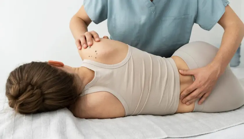 Fizjoterapeuta masuje odcinek lędźwiowy kręgosłupa pacjentki, pomagając w leczeniu dyskopatii lędźwiowej.