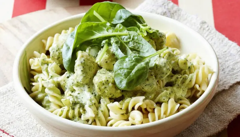 Pyszny makaron z kurczakiem w kremowym sosie pesto, udekorowany świeżym szpinakiem. Idealny obiad dla całej rodziny.