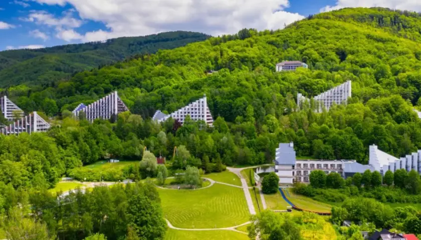 Nowoczesne budynki architektoniczne wkomponowane w zielone zbocza Beskidu Śląskiego. Uzdrowisko w Beskidzie Śląskim otoczone bujną roślinnością.