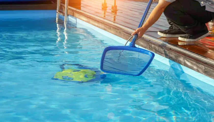 Mann reinigt den Pool mit einem Kescher. Ein gelbes Spielzeug schwimmt im klaren Wasser.