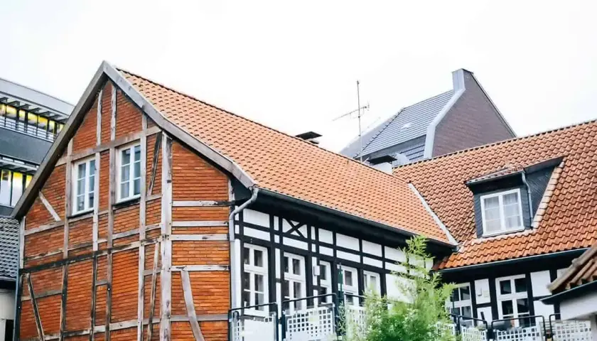 Urokliwy dom szachulcowy z ceglanymi ścianami i białymi belkami, otoczony innymi budynkami.