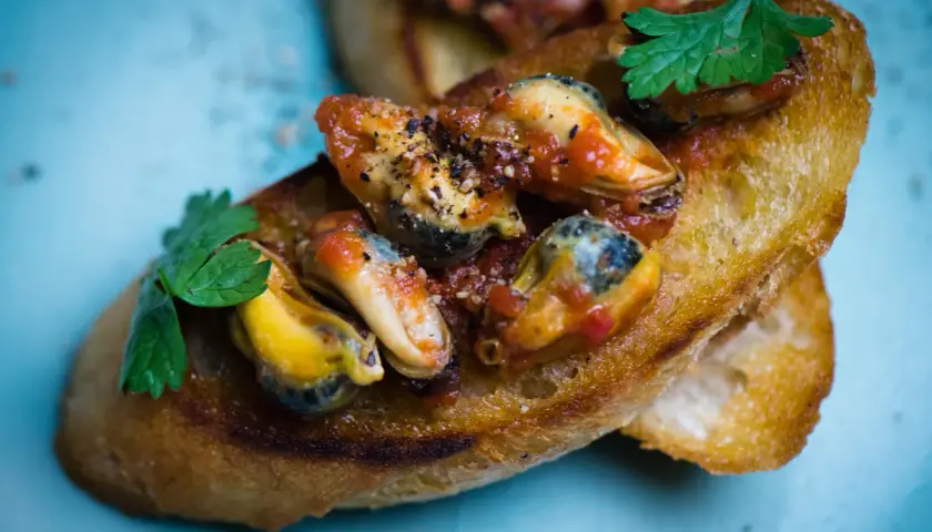 Chrupiące grzanki z soczystymi mule w pomidorach, ozdobione natką pietruszki. Pyszna przekąska.
