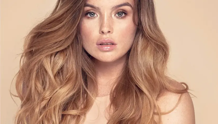 Mujer con cabello largo y ondulado, con un balayage inverso que va de castaño oscuro a rubio miel.