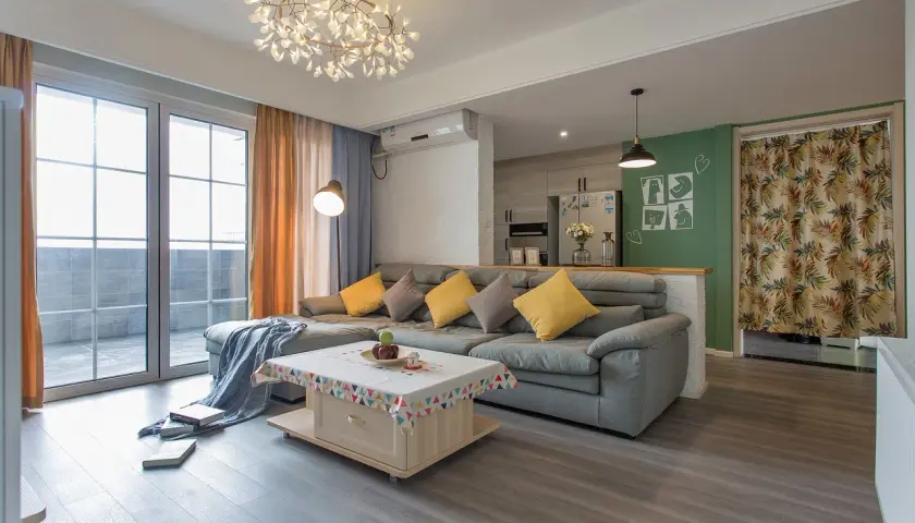 Nowoczesne oświetlenie pokoju tworzy przytulną atmosferę. W centralnym punkcie wisi designerska lampa, a obok niej stojąca lampa rzuca ciepłe światło na szarą sofę.