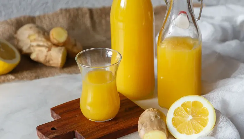 Ingwerwasser kochen oder nicht? Frischer Ingwer, Zitrone und goldgelbes Ingwerwasser in Flaschen und Glas.
