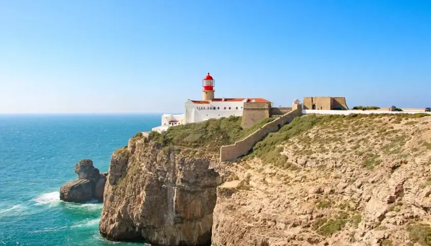 Lighthouse on a cliff overlooking the ocean, part of the fisherman's trail Portugal. Rugged coastline with a stone wall leading to the fort.