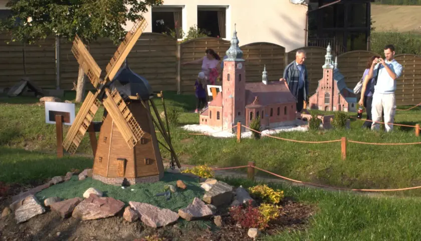 Drewniany wiatrak i kościółek w miniaturze, jakby z bajki. Strysza buda w tle, a obok ludzie podziwiający makietę.