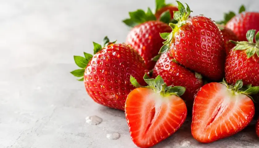 Fragole succose, ricche di potassio, su sfondo grigio. Una tagliata rivela la polpa rossa e i semini.