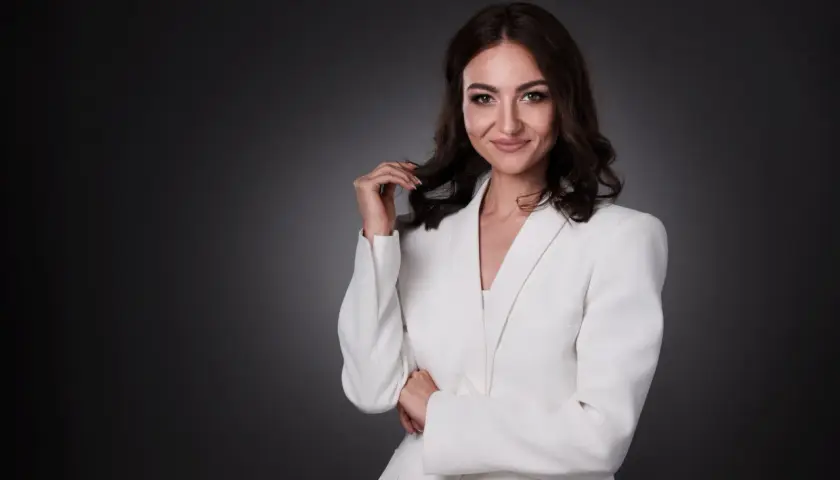 Elegancka kobieta w białej marynarce, uśmiecha się pewnie. To profesjonalne zdjecie biznesowe.