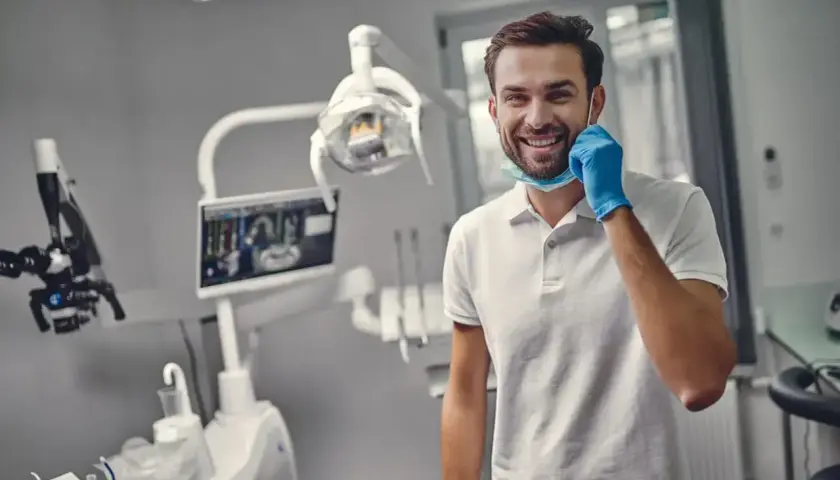Uśmiechnięty dentysta w gabinecie, gotowy do pracy. Zastanawiasz się, ile trwa plombowanie zęba? Krótka wizyta i zdrowy uśmiech!