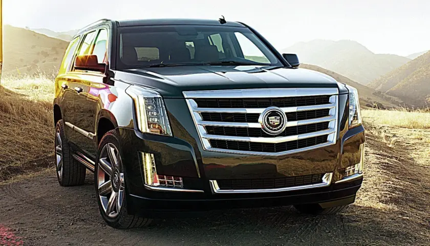 Ciemny Cadillac Escalade na tle gór i suchej trawy.