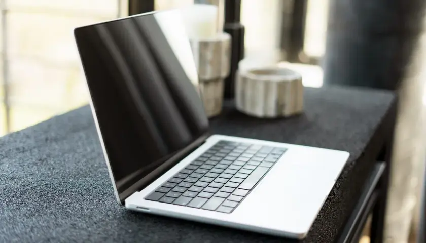 Otwarty MacBook na czarnym blacie. Dowiedz się, jak zmienić język w MacBook, aby dostosować go do swoich potrzeb.