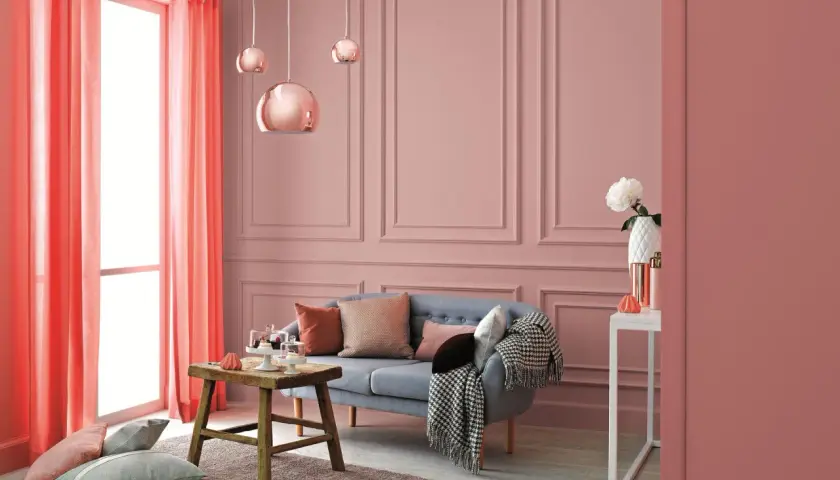 Przytulne, ciepłe wnętrza aranżacje w odcieniach różu i koralu. Sofa, stolik, poduszki i zasłony tworzą przytulną atmosferę.