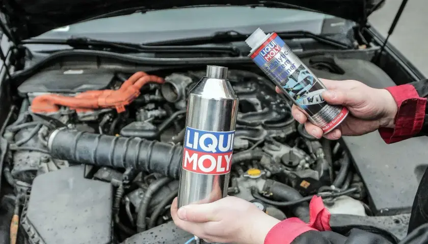 Ręce trzymają preparat do czyszczenia katalizatora diesel marki Liqui Moly. W tle widać silnik samochodu.