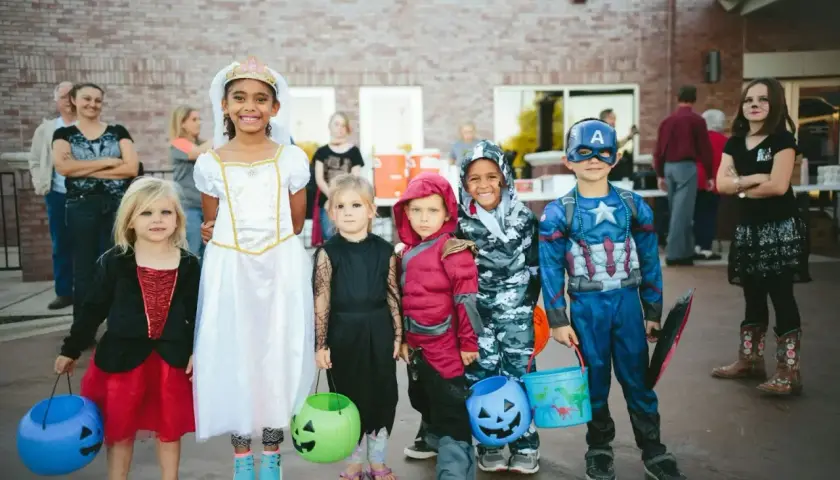 Dzieci w strojach na Halloween, gotowe na psikusy i zbieranie słodyczy. Wśród nich księżniczka, Kapitan Ameryka i inne postacie.