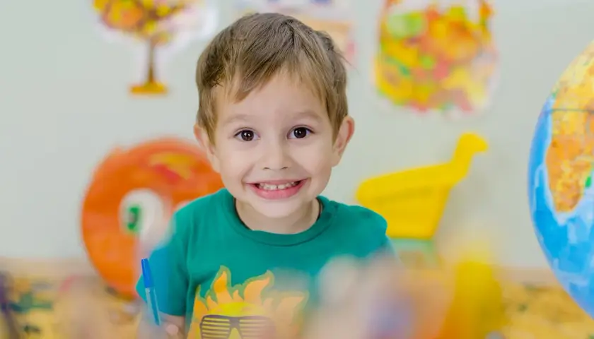 Niño sonriente con camiseta verde, rodeado de objetos coloridos. Fomenta la autoestima en niños con actividades creativas.