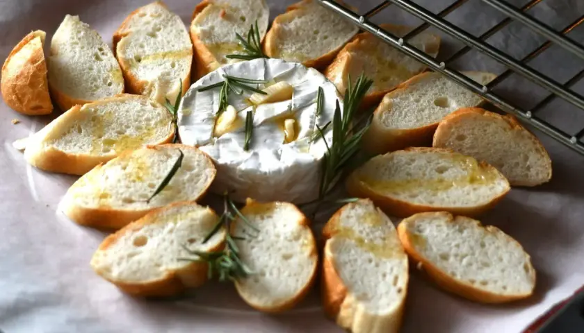 Pyszny, pieczony camembert z czosnkiem i rozmarynem, otoczony kromkami bagietki. Idealna przekąska na ciepło.