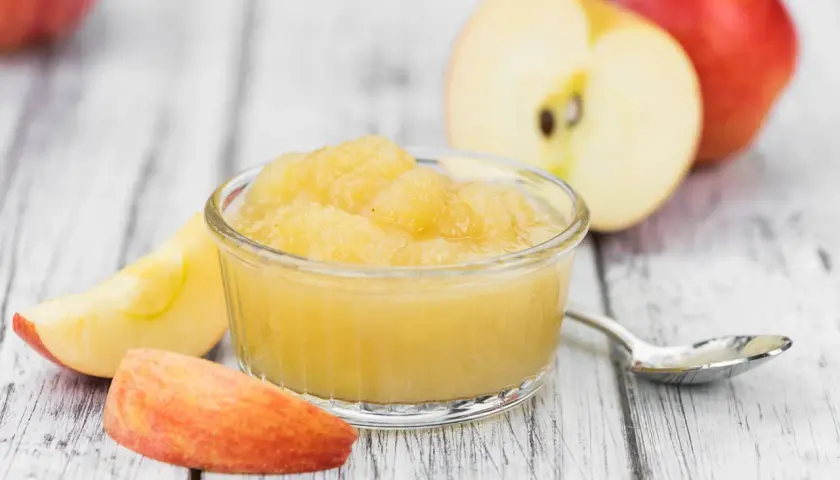 Apfelmus in einer Schale, umgeben von Apfelstücken und ganzen Äpfeln. Perfekt für leckere Rezepte mit Apfelsaft.