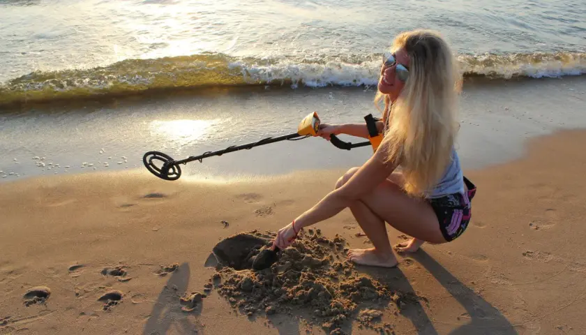 Dziewczyna z wykrywaczem metali na plaży. Czy można chodzić z wykrywaczem po plaży? Ona właśnie kopie w piasku, szukając skarbów.