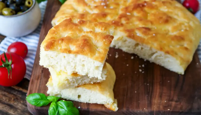 Frisch gebackene Focaccia, ein köstliches original focaccia rezept, mit Tomaten, Oliven und Basilikum auf einem Holzbrett.