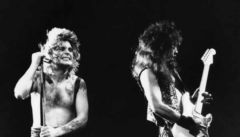 Ozzy Osbourne z mikrofonem i gitarzysta na scenie. Ikoniczny wokalista, znany z kontrowersyjnych występów, niczym ozzy osbourne bat, w swoim żywiole.