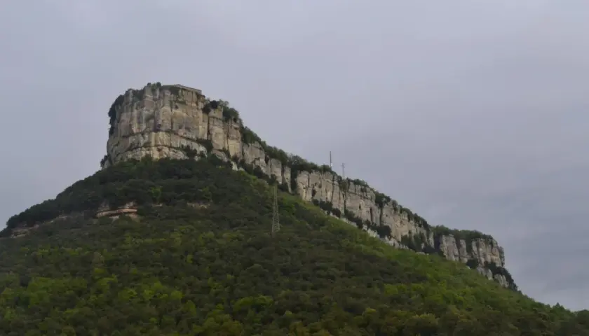 Imponent roca amb vegetació verda i una construcció al cim, recordant la Mare de Déu del Far.