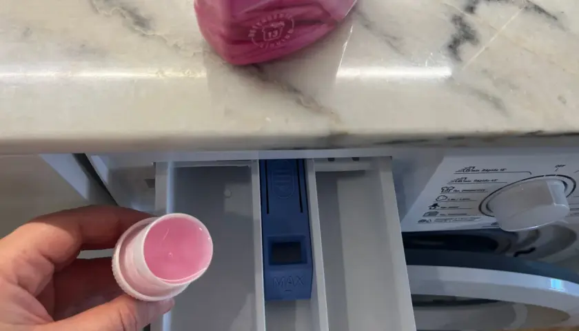 Hand hält Dosierkappe mit rosa Flüssigkeit. Waschpulver direkt in die Trommel geben? Nein, hier in die Schublade.