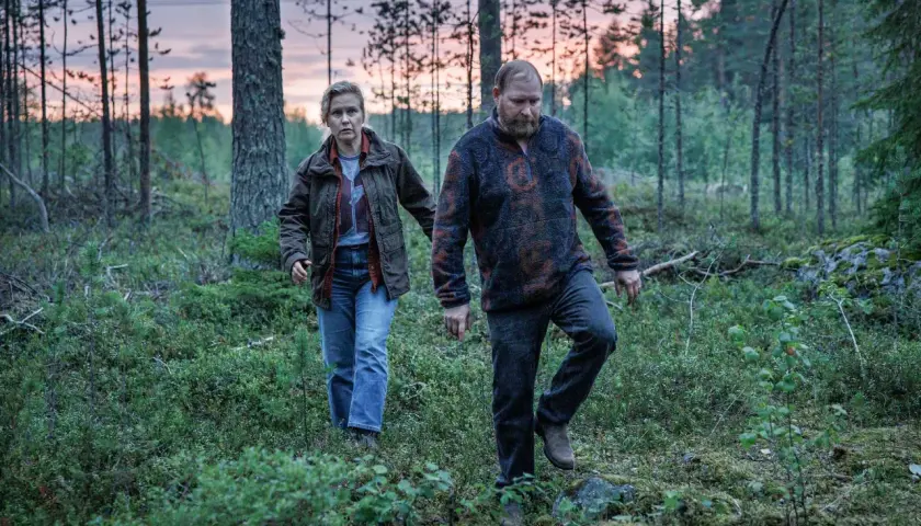 Två personer går genom en skog i skymningen. Det är en scen från Vargasommar del 2.
