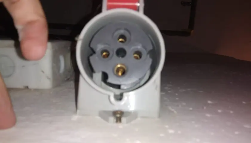 Zbliżenie na gniazdo do podłączenia wtyczki siłowej. Widoczne styki i mechanizm zabezpieczający.