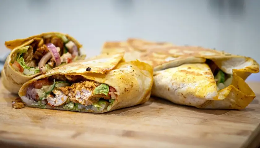 Pyszny kebab w tortilli z kurczakiem, warzywami i cebulą, ułożony na desce.