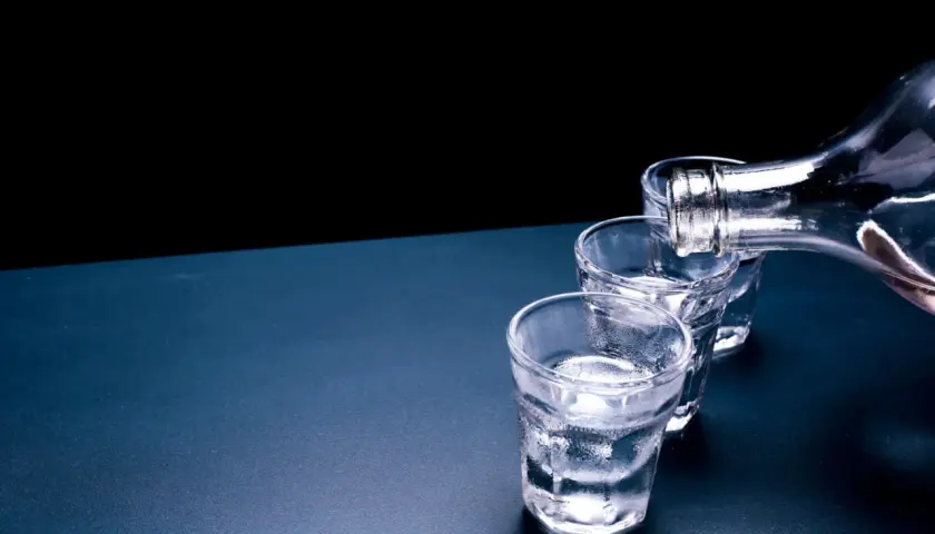 Ciepła wódka, dlaczego temperatura wpływa na odbiór paliwa? Trzy kieliszki wypełniane z butelki.