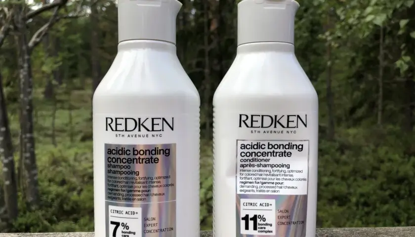 Två flaskor Redken Acidic Bonding Concentrate, schampo och balsam, står utomhus. Perfekt för att reparera skadat hår efter färgning.