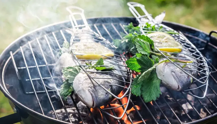 Deux poissons entiers sur un barbecue au charbon, garnis de citron et d'herbes fraîches, fumant doucement. Quel poisson au barbecue charbon !