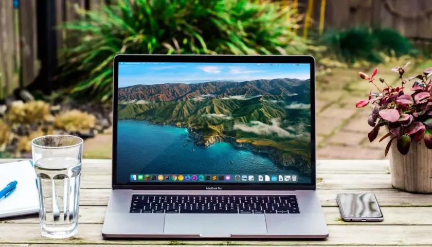 MacBook Pro z widokiem na wybrzeże Kalifornii. Obok szklanka wody, notatnik i telefon. Wiele marek laptopów oferuje podobne możliwości.