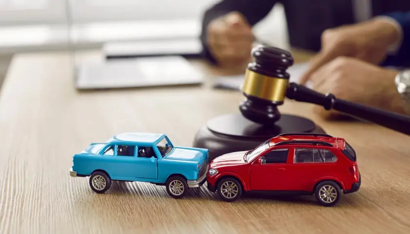 Modellini di auto blu e rossa che simulano un **infortunio in itinere** di circa 30 minuti, con un martelletto da giudice sullo sfondo.