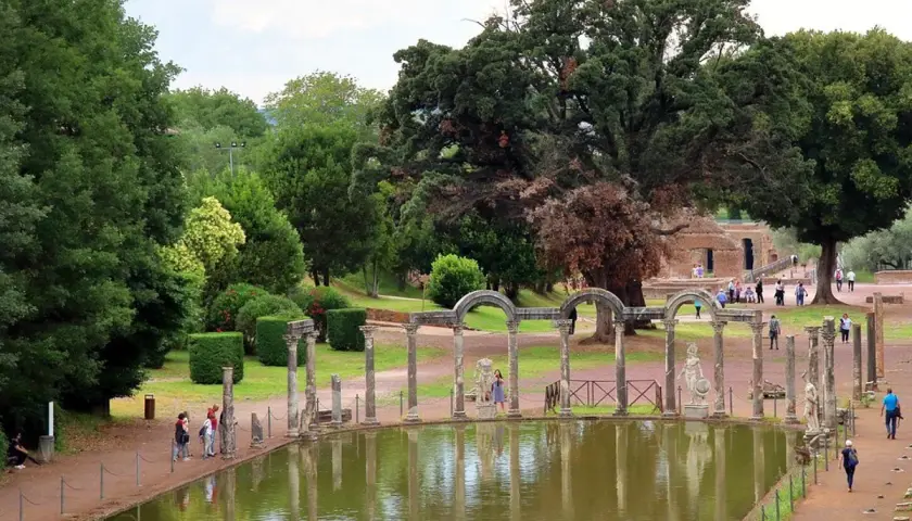 Vestiges antiques et étang reflétant le ciel à la Villa Adriana de Tivoli. Des colonnes romaines bordent l'eau, entourées de verdure luxuriante.